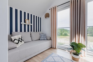 Ein modernes Wohnzimmer mit einer Couch, einer Pflanze, einem Fenster mit Vorhängen und einer gestreiften Wand.