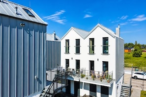 A modern building with a white facade, multiple windows, and a balcony with outdoor seating. - Komfortowy dom nad morzem (Jastrzębia Góra)