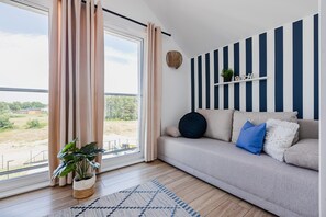Una sala moderna con un sofá, una planta en maceta y vistas a través de un ventanal.