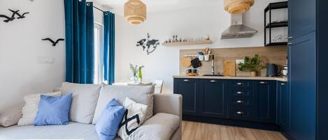 A modern living room with a sofa, kitchen area, and decorative elements like a world map and bird wall art.