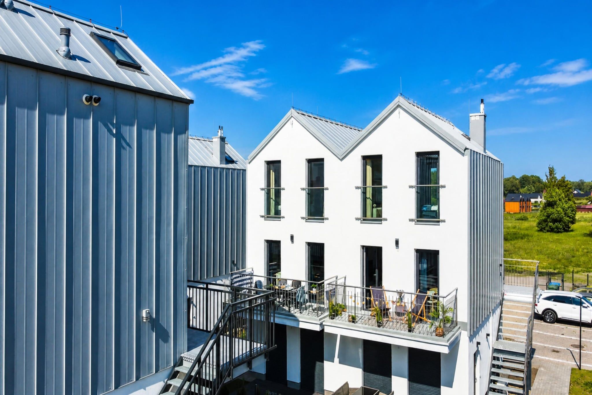 Un bâtiment moderne à la façade blanche, doté de nombreuses fenêtres et d’un balcon avec des sièges pour l’extérieur.