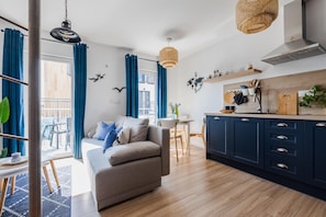 Ein modernes Wohnzimmer mit Sofa, Esstisch und Küchenzeile mit Schränken und einer Pendelleuchte.