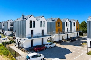 Une rangée d’immeubles modernes à plusieurs étages, avec un espace de stationnement devant.