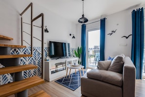 Un salon moderne avec un téléviseur, un canapé, un escalier en bois et un balcon agrémenté de rideaux bleus.
