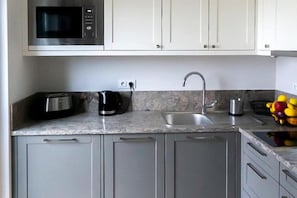 A kitchen with a microwave, toaster, kettle, sink, and a fruit bowl.