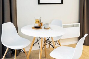A small round table with a coffee maker and a cup, flanked by two white chairs.