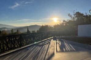 A balcony with a view of mountains and the sun setting.