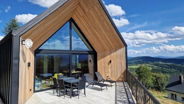 Une maison moderne dotée d’une grande baie vitrée, d’une terrasse en bois et offrant une vue sur la campagne.