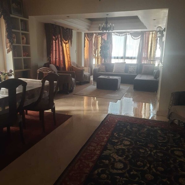 A spacious living room with a dining area, a chandelier, and a large window with curtains.