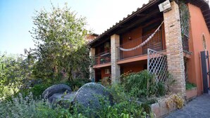 A two-story building with a balcony, stone pillars, and a garden with rocks and plants. - Tower mini suite in historic farmhouse steps from lake beach (Lazio)