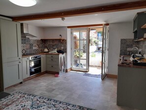 Une cuisine avec un mur recouvert de carreaux, des meubles en bois, un four encastré et une grande porte-fenêtre coulissante donnant sur un espace extérieur.