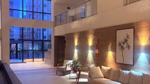 En rymlig entréhall med högt i tak, en soffa, stolar, en krukväxt och ett inramat konstverk på väggen.