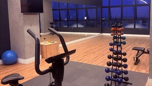 Ett gym med en motionscykel, ett ställ med hantlar och ett stort fönster med utsikt över staden.