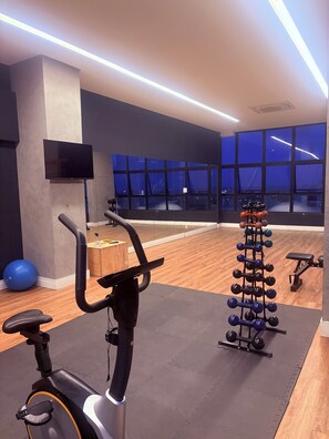A gym with an exercise bike, a rack of dumbbells, and a large window with a city view. - High standard near the American consulate and in the heart of the capital of Pernambuco. (Recife)