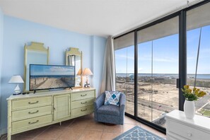 Ein Zimmer mit großem Fenster, Fernseher, Kommode, Stuhl und Blick auf eine Baustelle.