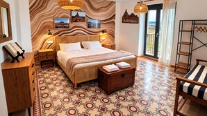 A bedroom with a large bed, a wooden headboard, a nightstand, a bedside table, a dresser, a patterned floor, a hanging light fixture, a window with a view, and a sign on the wall.