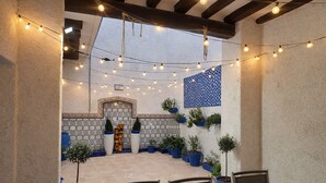 An outdoor patio with string lights, potted plants, and a tiled wall with a decorative pattern.