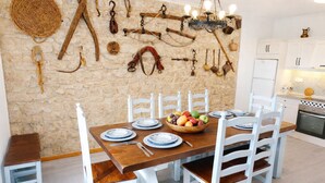 A dining area with a stone wall, wooden table, white chairs, and a fruit bowl.