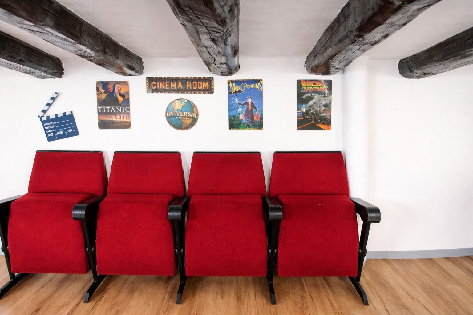 Una sala de cinema amb seients vermells, bigues de fusta al sostre i pòsters de pel·lícules a la paret.