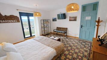 A bedroom with a bed, a bench, a TV, a door, and a view of the outdoors.