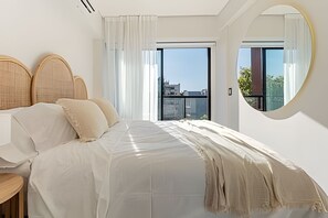 Ein modernes Schlafzimmer mit einem großen Bett, einem runden Spiegel und Blick auf die Stadtlandschaft durch das Fenster.