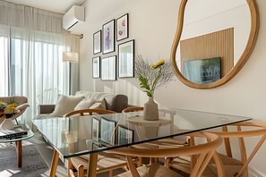 Ein modernes Wohnzimmer mit einem Glastisch, Holzstühlen, einer Couch und einem großen Spiegel.