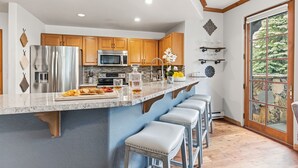 Una cocina con armarios de madera, electrodomésticos de acero inoxidable, encimera de mármol y un amplio ventanal con pared de piedra.
