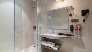 Un baño moderno con cabina de ducha de vidrio, lavamanos de mármol, un espejo grande y un secador de pelo fijado en la pared.