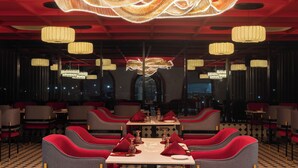 Un restaurante con una mesa central, sillas tapizadas en rojo y una escultura iluminada en el techo.