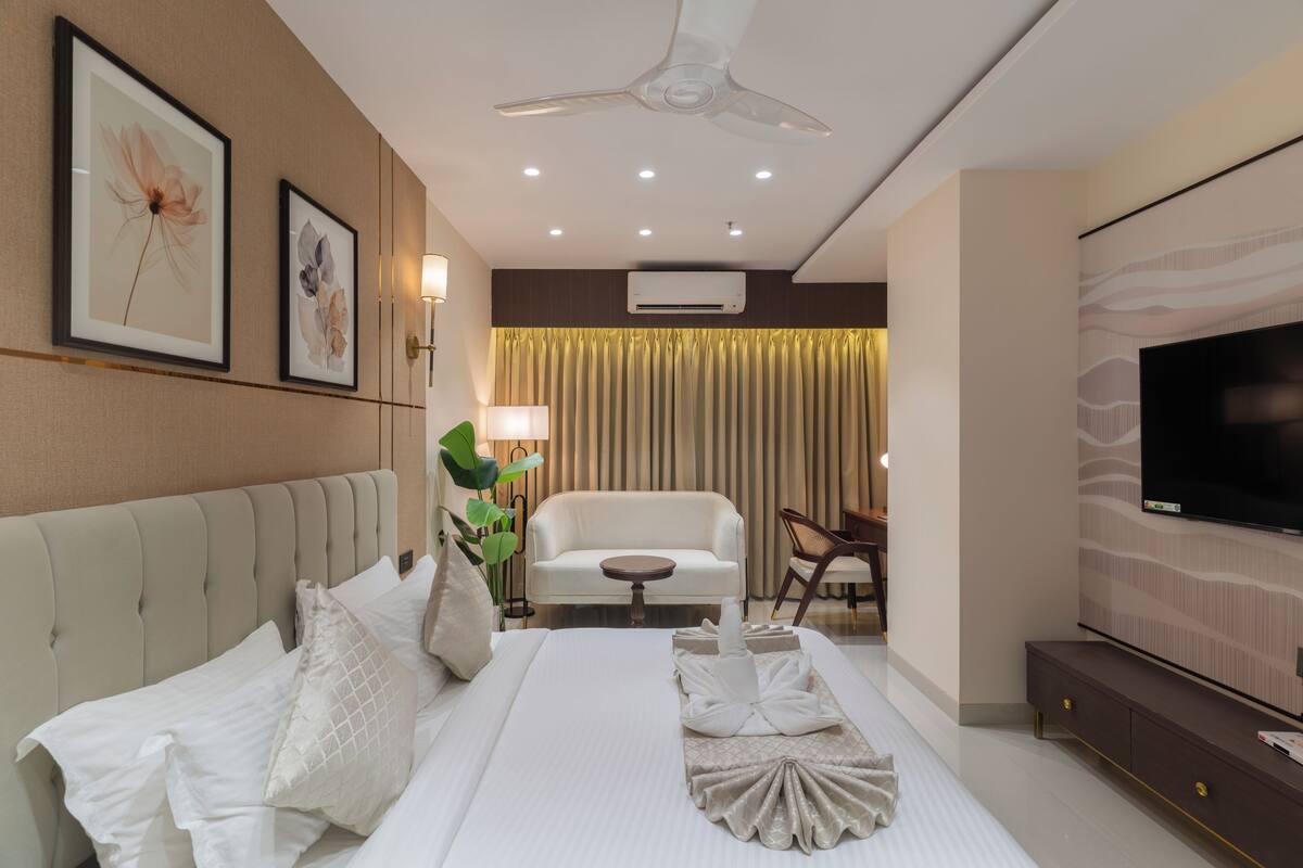 Una habitación de hotel con cama, sofá, televisión y ventilador de techo.