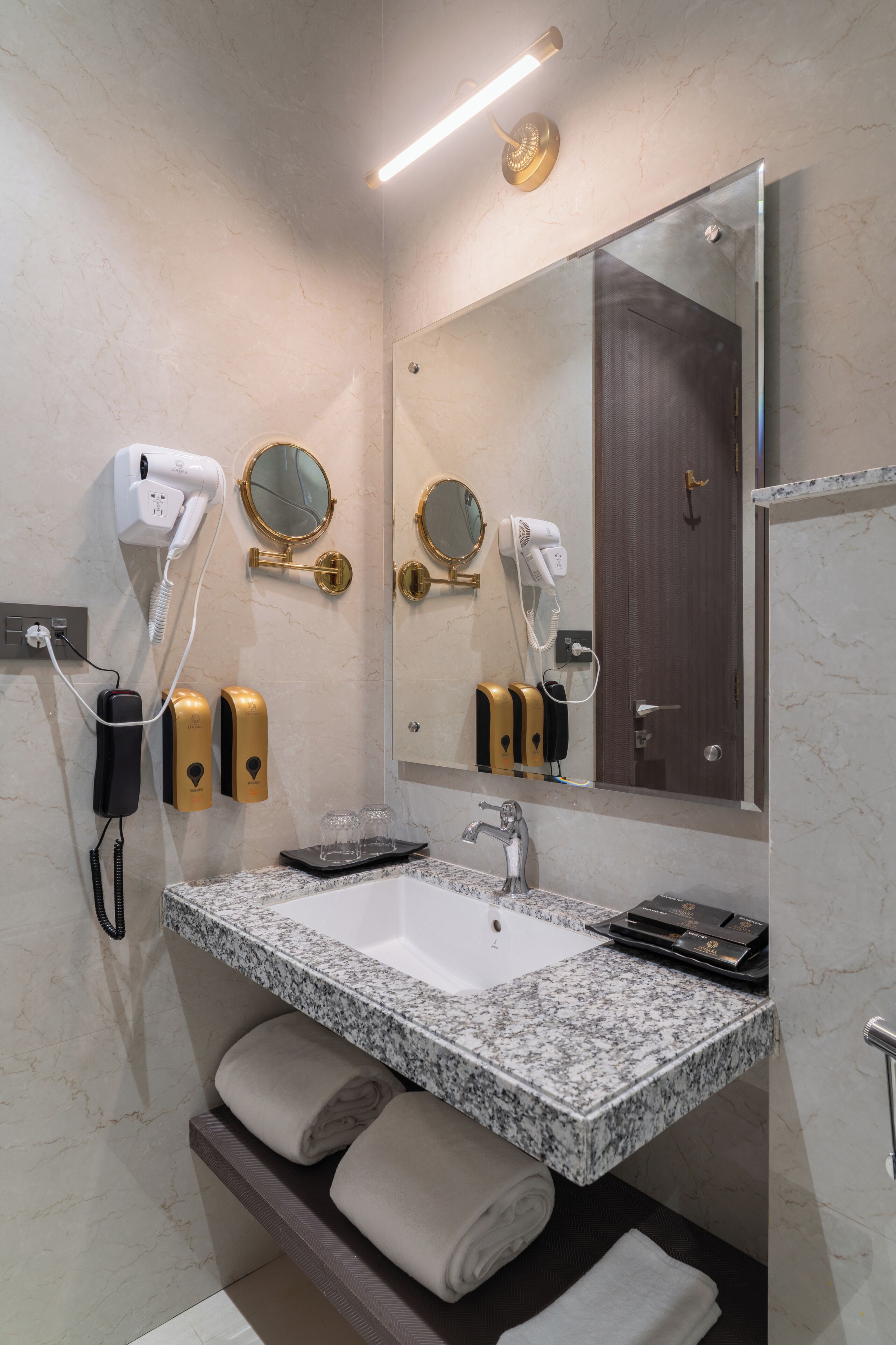 A modern bathroom with a marble sink, two hair dryers, and a large mirror.