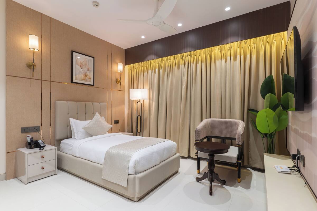 Habitación de hotel con cama, mesita de noche, lámpara, silla y un espejo grande.