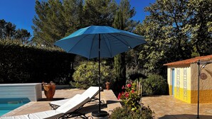 Et poolområde med liggestol, blå parasol og en potteplante.