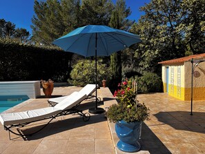 Ein Poolbereich mit Liegestuhl, blauem Sonnenschirm und einer Topfpflanze.