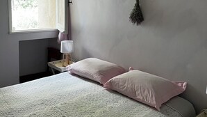 Et soveværelse med seng, et vindue, et natbord og en lampe på væggen.