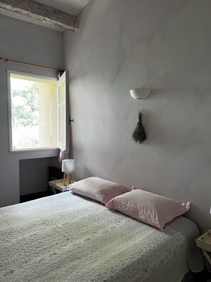 Ein Schlafzimmer mit Bett, Fenster, Nachttisch und einer Wandlampe.