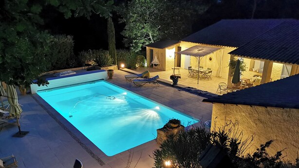 En swimmingpool med liggestole, en overdækket terrasse og en bygning i sten.