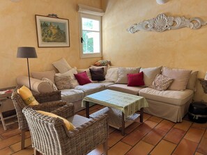Ein gemütliches Wohnzimmer mit einer Couch, Korbstühlen, einem Tisch, einer Lampe und einem Gemälde an der Wand.