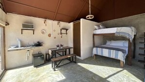 A compact room with a bunk bed, a small kitchenette, a wooden table, and a bench.