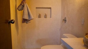 A bathroom with a toilet, a towel hanging on the wall, and two bottles on a shelf.