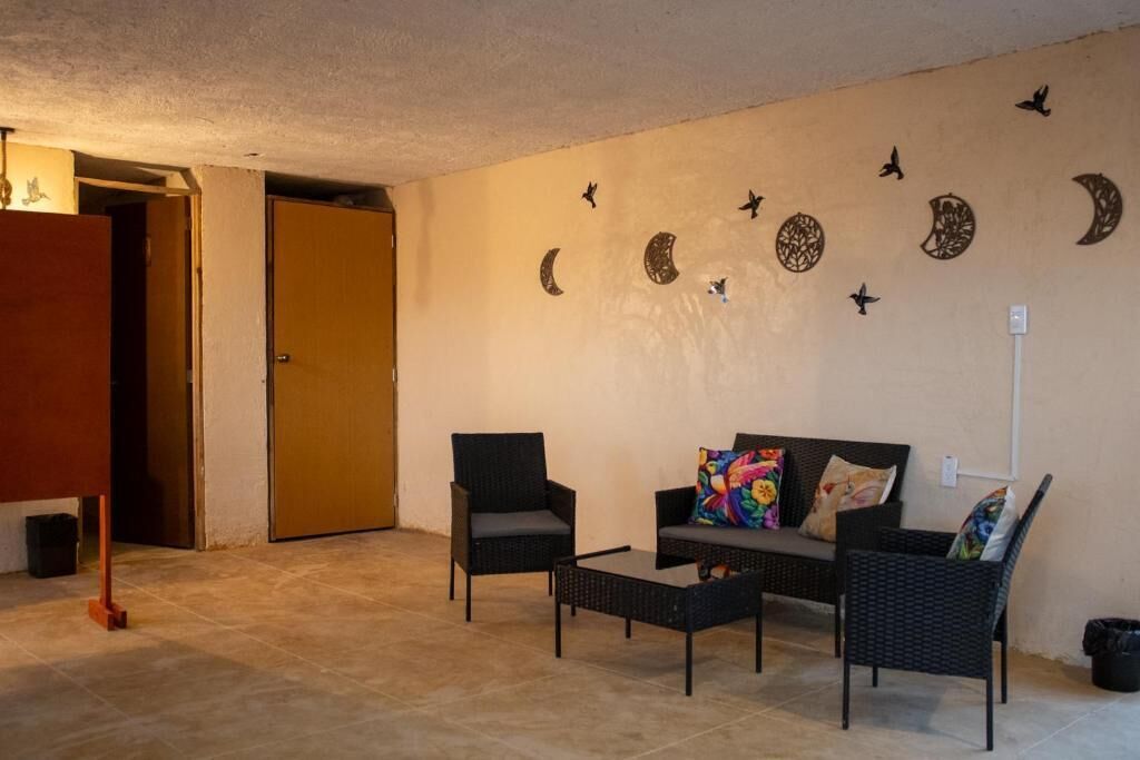 Une pièce comprenant un canapé, deux fauteuils, une table basse, une porte et des éléments de décoration murale, notamment des motifs d’oiseaux et de lunes.
