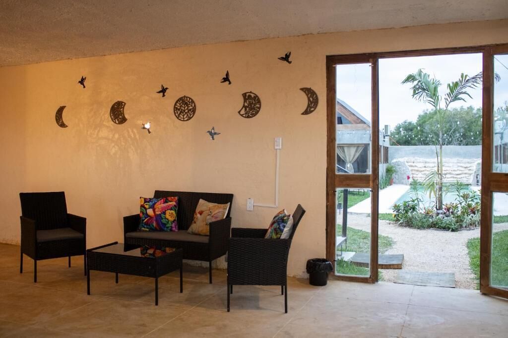 Ein Wohnzimmer mit einer Couch, zwei Sesseln, einem Couchtisch und einer Glastür, die zu einem Garten führt.