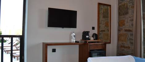 Une chambre d’hôtel avec un lit, un téléviseur à écran plat fixé au mur, un bureau avec une machine à café et un mur en pierre.