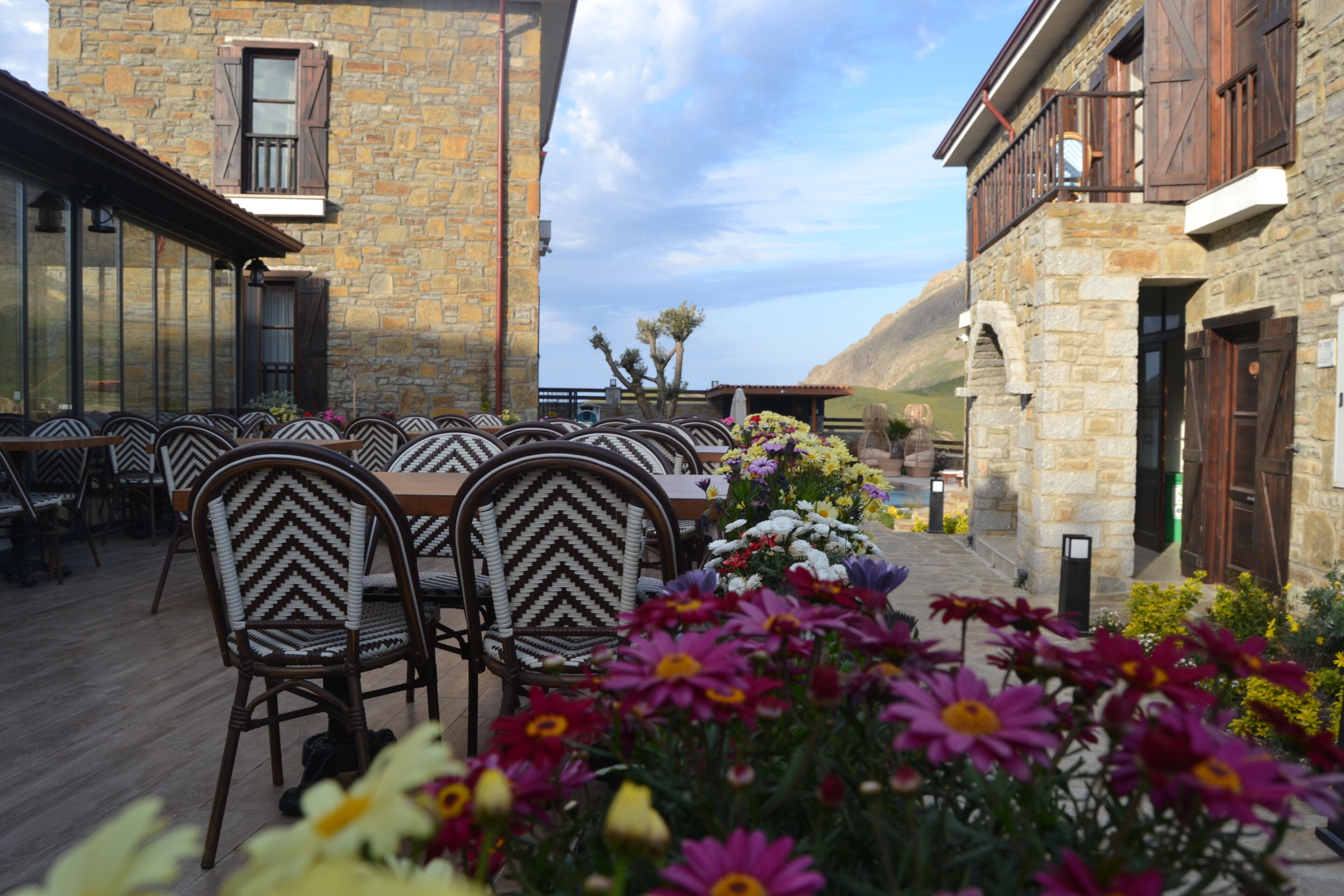 Un espacio de comedor al aire libre con edificios de piedra, sillas de mimbre y una variedad de flores.