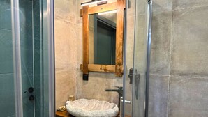 Un baño con lavamanos de piedra, espejo con marco de madera y cabina de ducha de cristal.