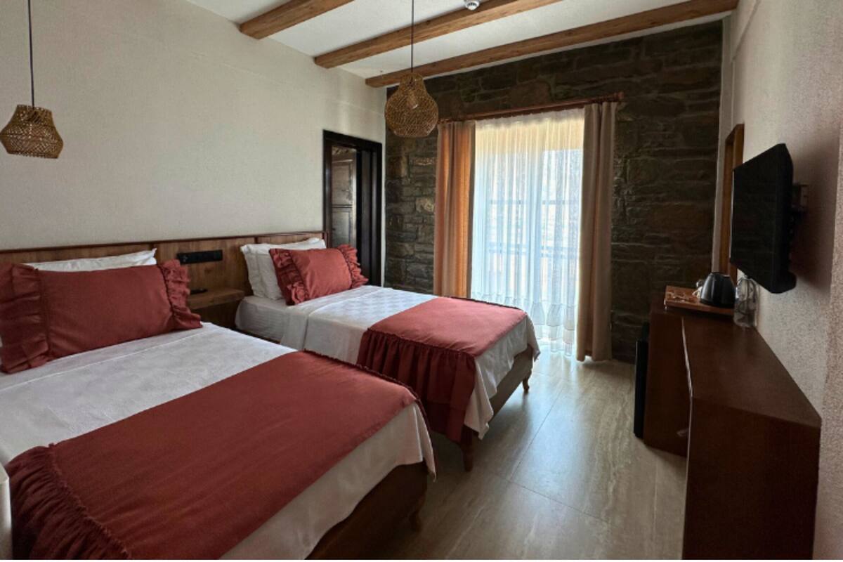A hotel room with two beds, a stone wall, a television, and a window with curtains.