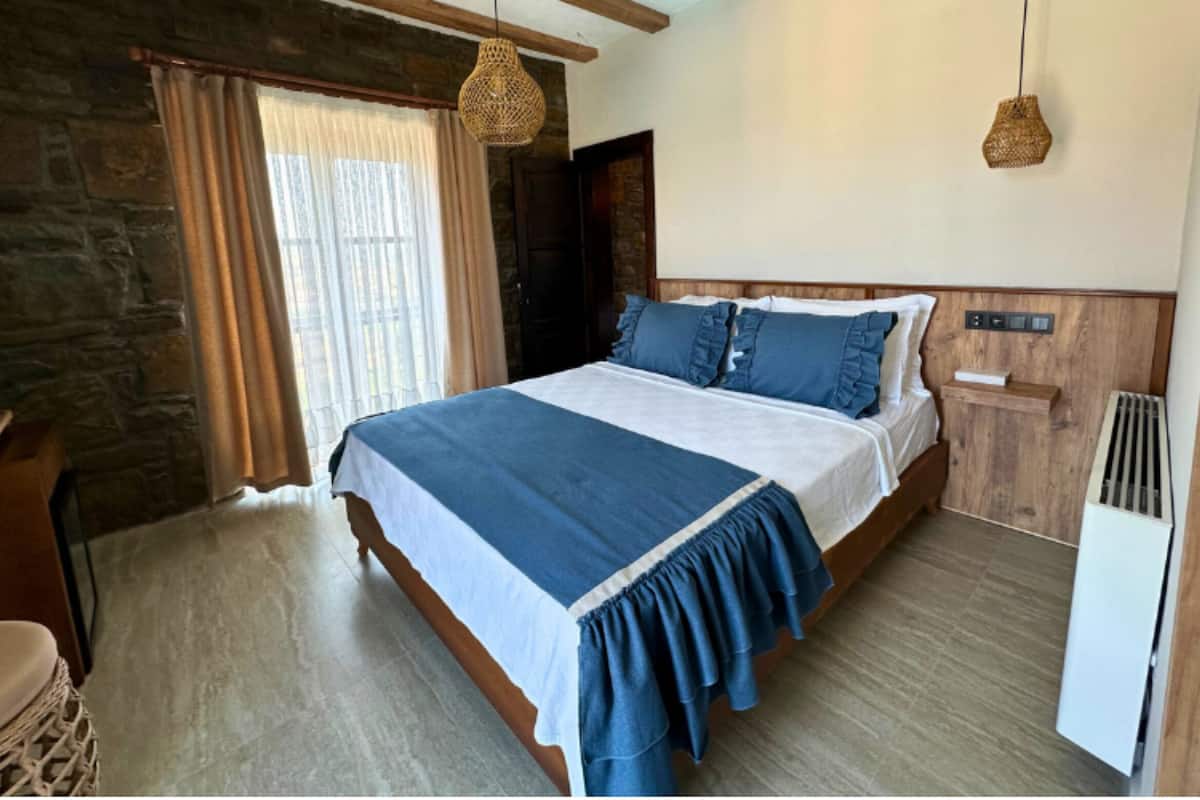 A bedroom with a bed, wooden headboard, stone wall, and a hanging light fixture.