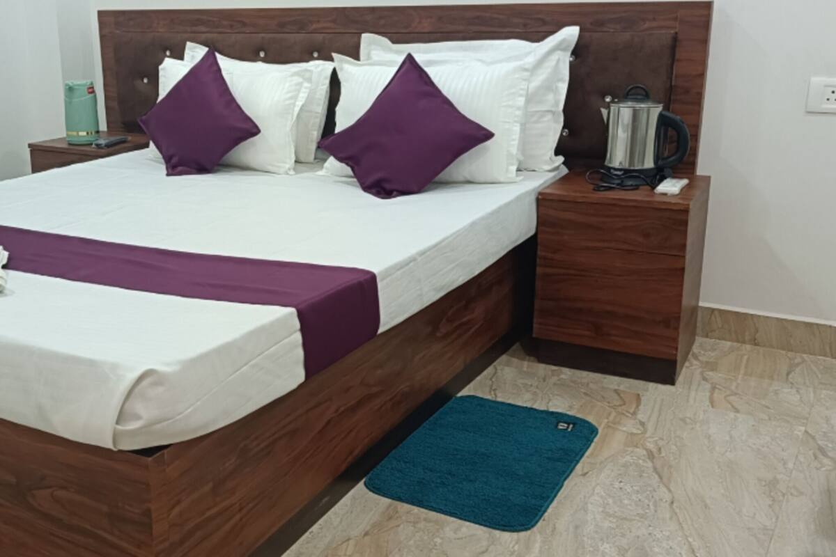 A neatly made bed with a white and purple bedspread, a wooden headboard, and a blue rug on the floor.