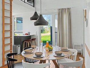 Ein Essbereich mit einem runden Tisch, weißen Stühlen und einer schwarzen Pendelleuchte. Durch eine Schiebetür bietet sich ein Blick auf einen Garten.