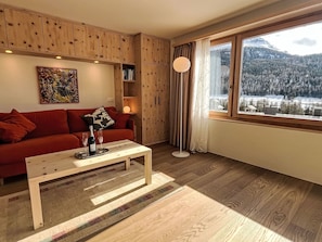 A modern living room with a red sofa, a wooden coffee table, and a large window with a mountain view. - Panorama - Chesa Roseg ÖV inklusive by Interhome (Pontresina)